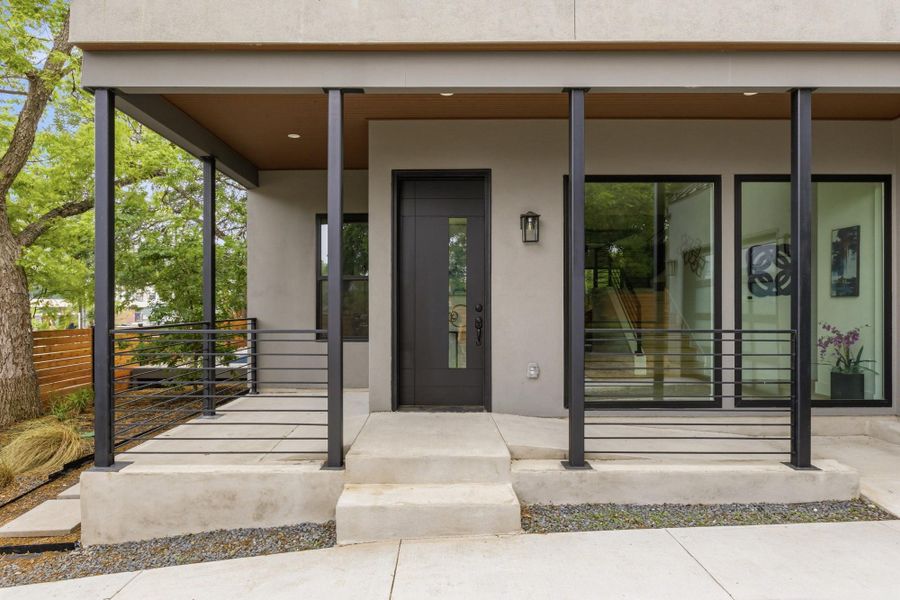 Modern exterior featuring a covered porch with black metal railings, a dark entry door with frosted glass, and large black-framed windows