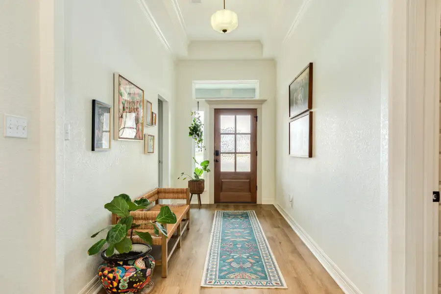 Bright and welcoming entryway featuring a wooden front door with glass panels, a beautiful light fixture, and wood look flooring. The space adds a cozy and inviting atmosphere.