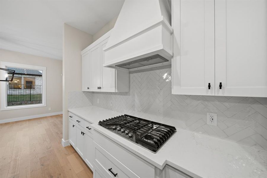 Kitchen featuring white cabinetry, premium range hood, light stone countertops, tasteful backsplash, and stainless steel gas stovetop
