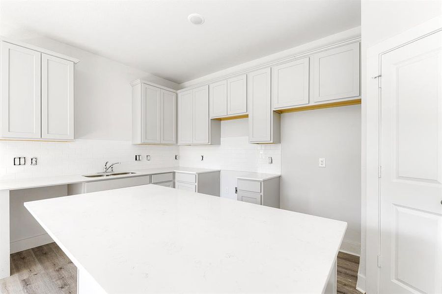 Quartz countertops, large working island, light gray cabinets, and subway tile backsplash.