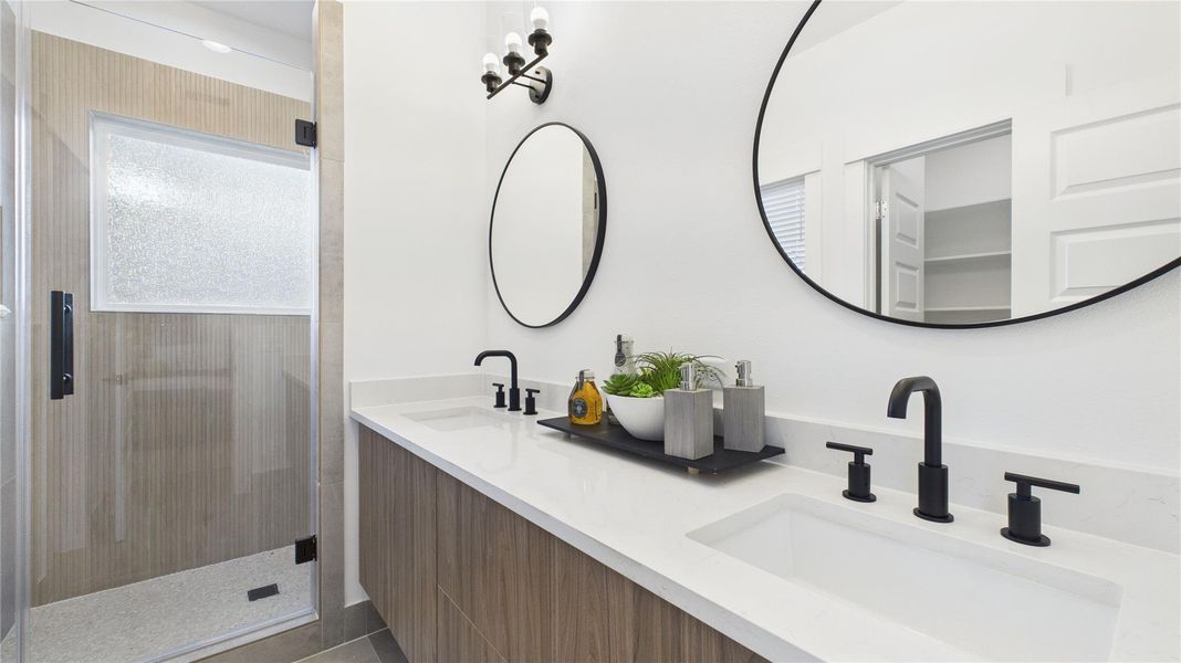 The luxurious primary ensuite features sleek modern finishes, a glass-enclosed shower with stylish tile, and a double-sink vanity topped with quartz countertops, complemented by two contemporary mirrors and lighting fixtures, creating a bright, elegant, and functional retreat.