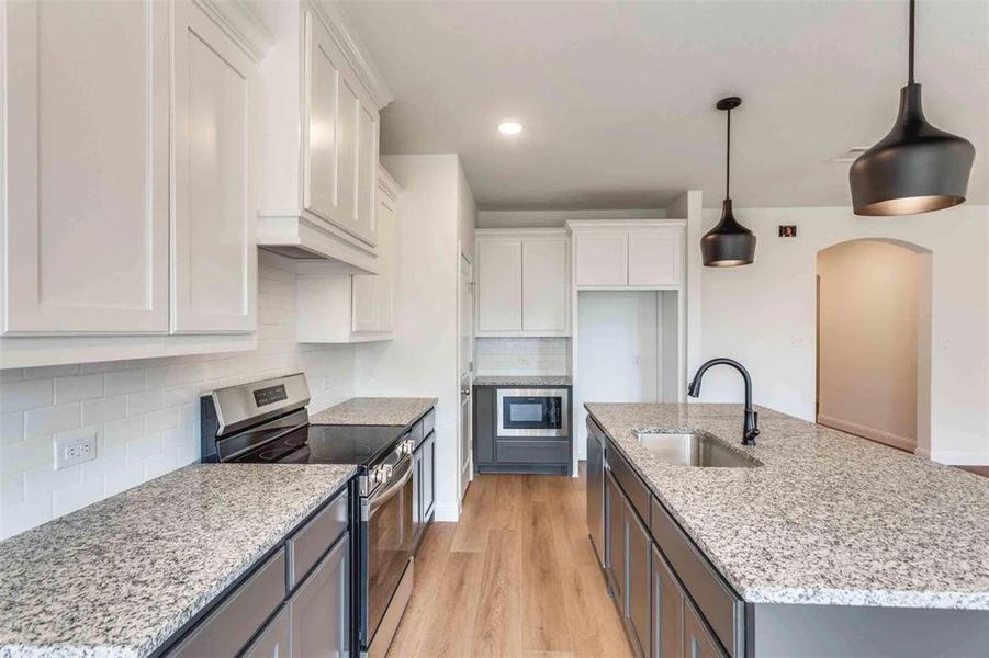 Kitchen featuring stainless steel appliances, a sink, white cabinets, decorative backsplash, and a kitchen island with sink