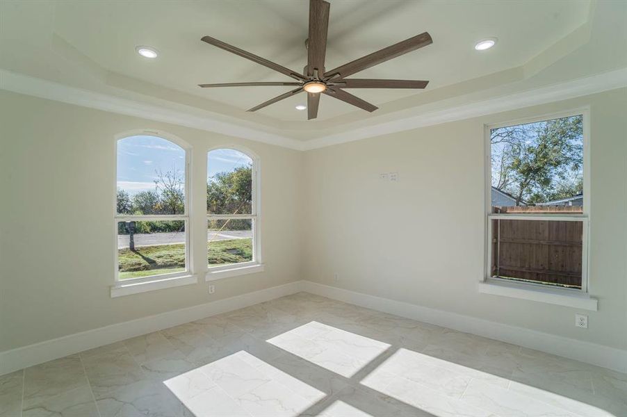Empty room featuring a tray ceiling, ornamental molding, and light marble finish flooring Empty room featuring a tray ceiling, ornamental molding, and light marble finish flooring