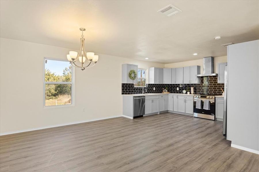 Kitchen featuring pendant lighting, white cabinetry, stainless steel appliances, wall chimney range hood, and light hardwood / wood-style flooring