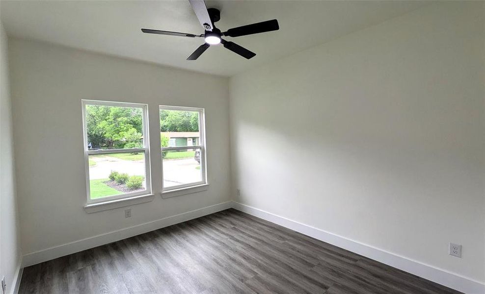 Empty room with dark wood-style flooring, baseboards, and a ceiling fan