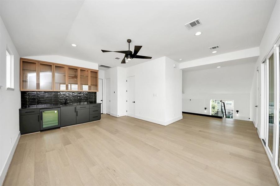 Spacious 3rd-floor game room featuring sleek wood flooring, a built-in wet bar with glass cabinetry, and modern finishes. This versatile space offers direct access to the rooftop terrace, perfect for entertaining or relaxing.