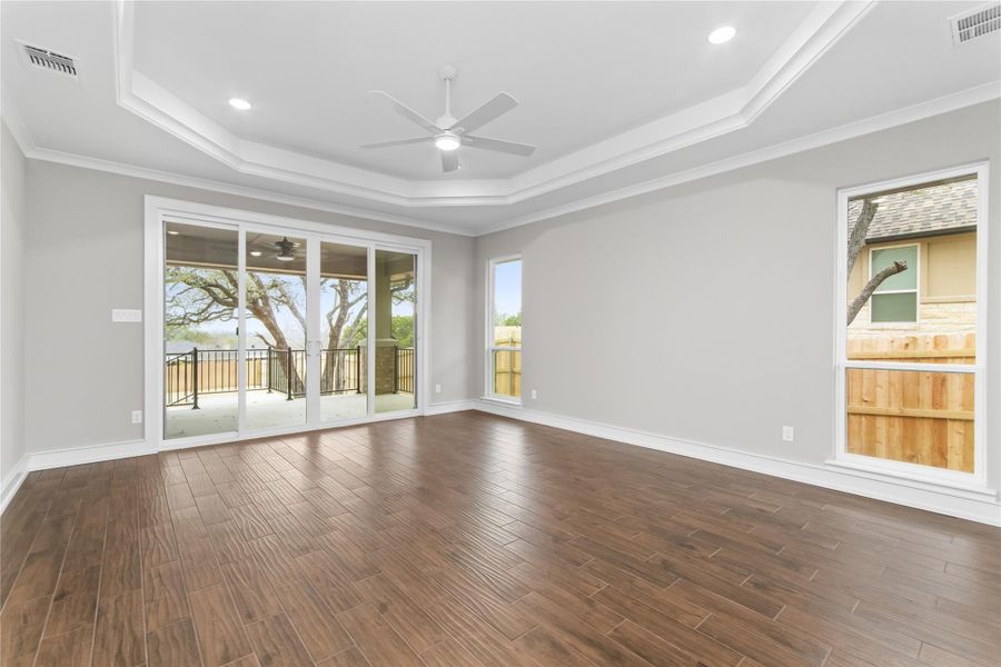 Spare room featuring ceiling fan, a raised ceiling, dark wood-style flooring, baseboards, and crown molding Spare room featuring ceiling fan, a raised ceiling, dark wood-style flooring, baseboards, and crown molding