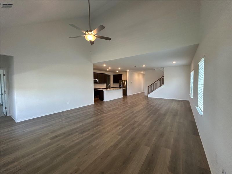 Unfurnished living room with stairway, dark wood-style flooring, recessed lighting, a ceiling fan, and a towering ceiling