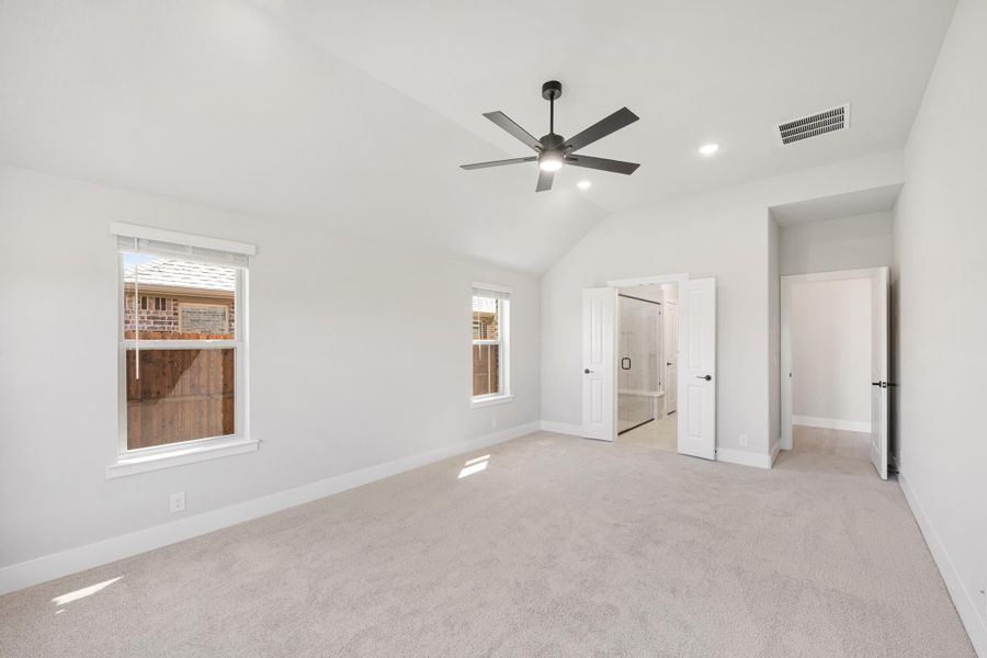 Spacious bedroom with vaulted ceiling, ceiling fan, carpet flooring, and open door to ensuite bathroom Spacious bedroom with vaulted ceiling, ceiling fan, carpet flooring, and open door to ensuite bathroom
