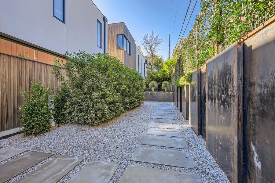A modern exterior showcases a clean pathway of pavers set in gravel, bordered by lush greenery and a striking metal fence. A modern exterior showcases a clean pathway of pavers set in gravel, bordered by lush greenery and a striking metal fence.