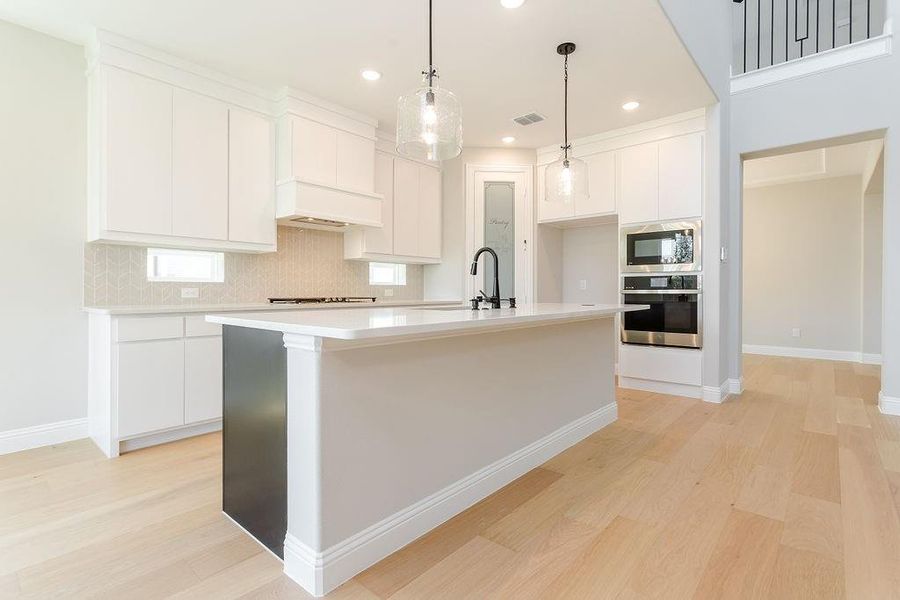 Kitchen featuring light hardwood / wood-style floors, oven, built in microwave, and an island with sink