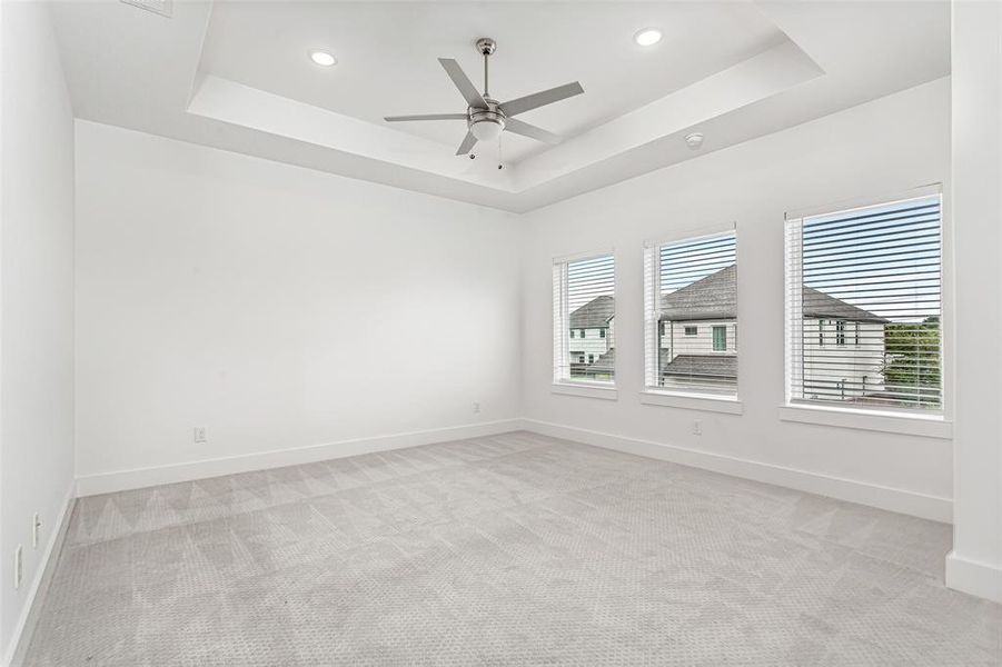 Unfurnished room with a raised ceiling, light carpet, recessed lighting, and ceiling fan
