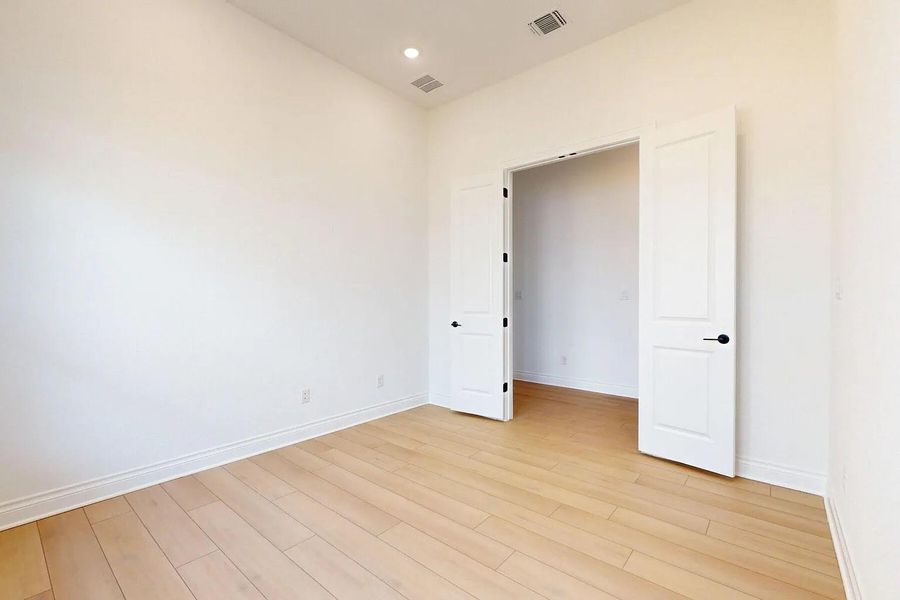 This room features light-toned wood flooring, clean white walls, and a recessed ceiling light