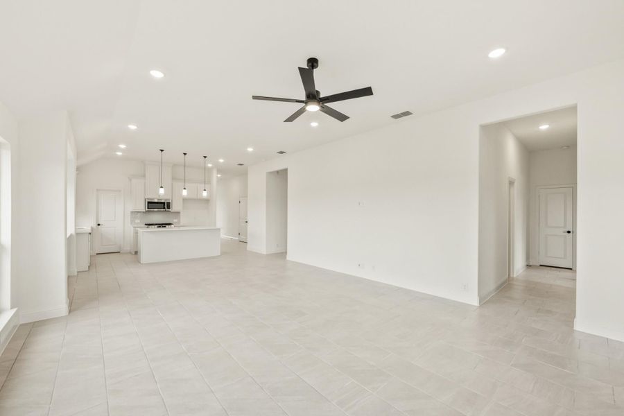 Open living area with tile floors and ceiling fan, open to white kitchen with island and pendant lights