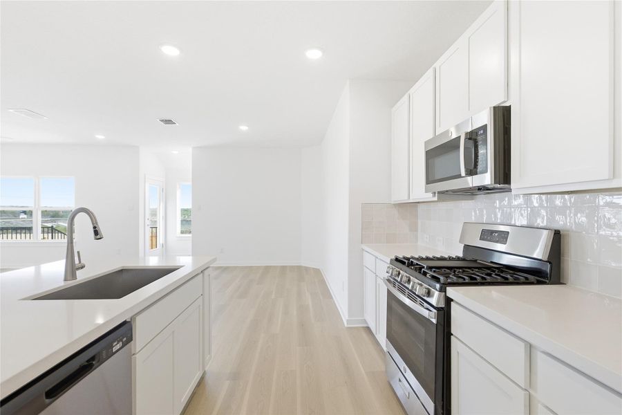Kitchen with stainless steel appliances, white cabinetry, light wood-style floors, tasteful backsplash, and recessed lighting