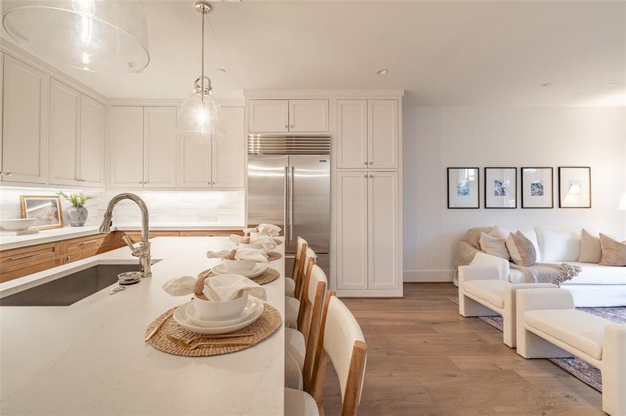 Kitchen with sink, white cabinetry, built in refrigerator, hanging light fixtures, and light hardwood / wood-style flooring