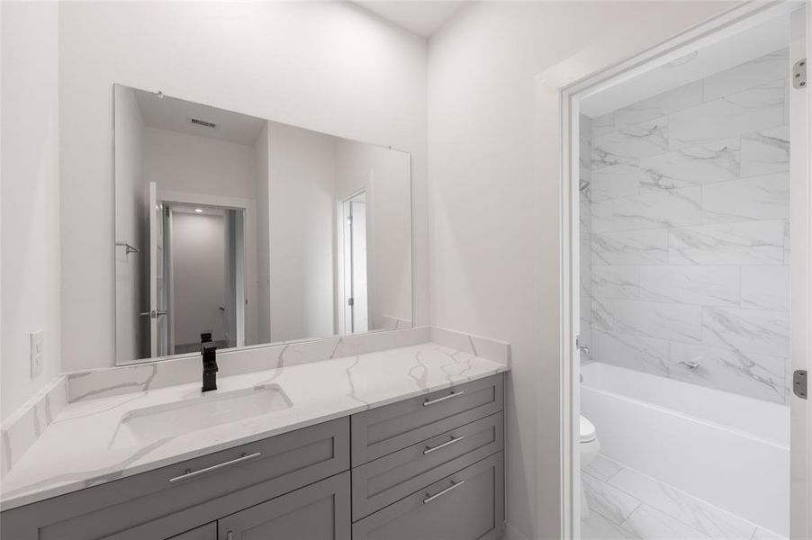 *Representative Photo. A modern bathroom with sleek gray cabinetry, a white marble countertop, large mirror, and tub shower.