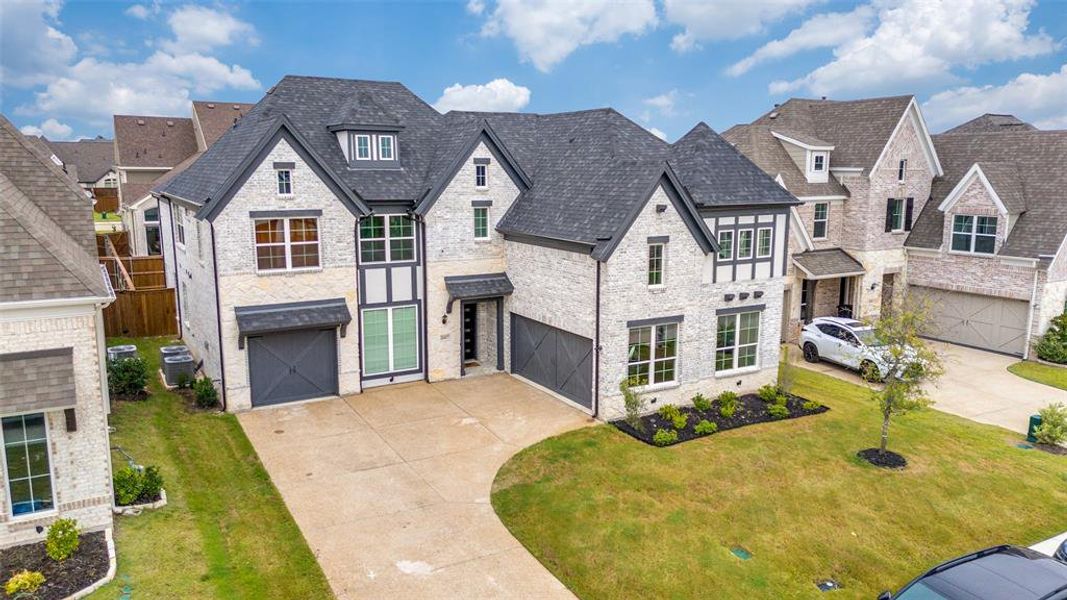 French country inspired facade with a residential view, driveway, stone siding, an attached garage, and a front yard