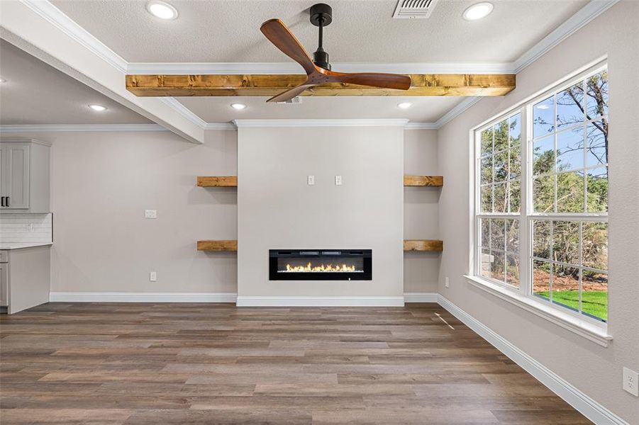 Unfurnished living room featuring ceiling fan, beamed ceiling, a healthy amount of sunlight, and wood-type flooring