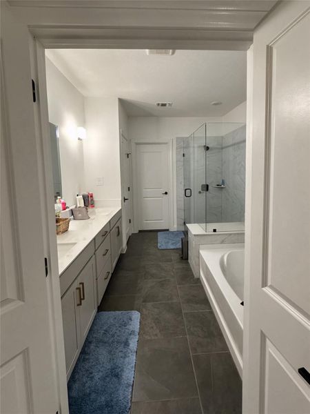 Expansive bathroom featuring a dual vanity with undermount sinks, a built-in bathtub, a glass-enclosed shower with tiled walls, and dark square floor tiles Expansive bathroom featuring a dual vanity with undermount sinks, a built-in bathtub, a glass-enclosed shower with tiled walls, and dark square floor tiles