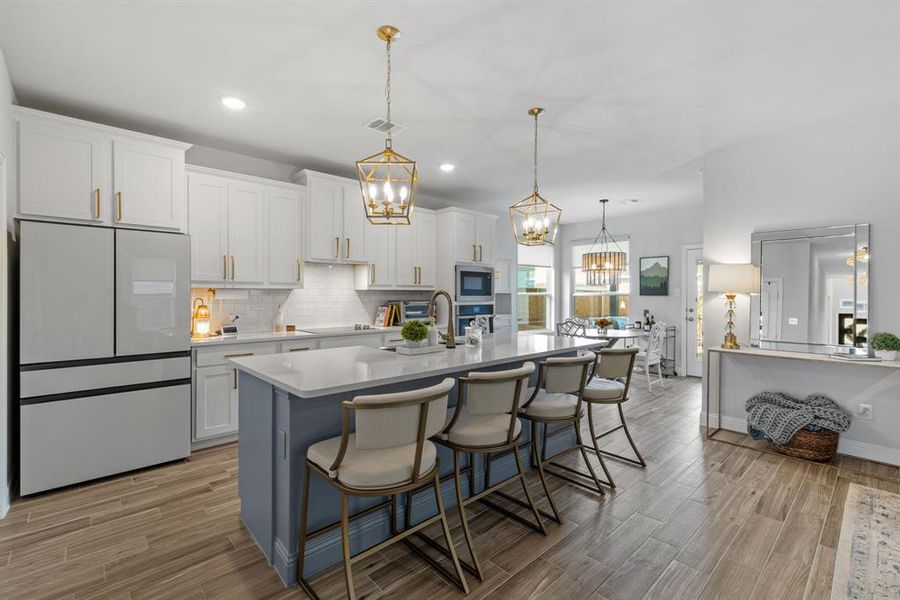 The kitchen features a sleek, included Samsung Bespoke refrigerator that blends modern technology with customizable style. White cabinets, a spacious breakfast bar, wood-look floors, and recessed lighting complete this bright and functional space.