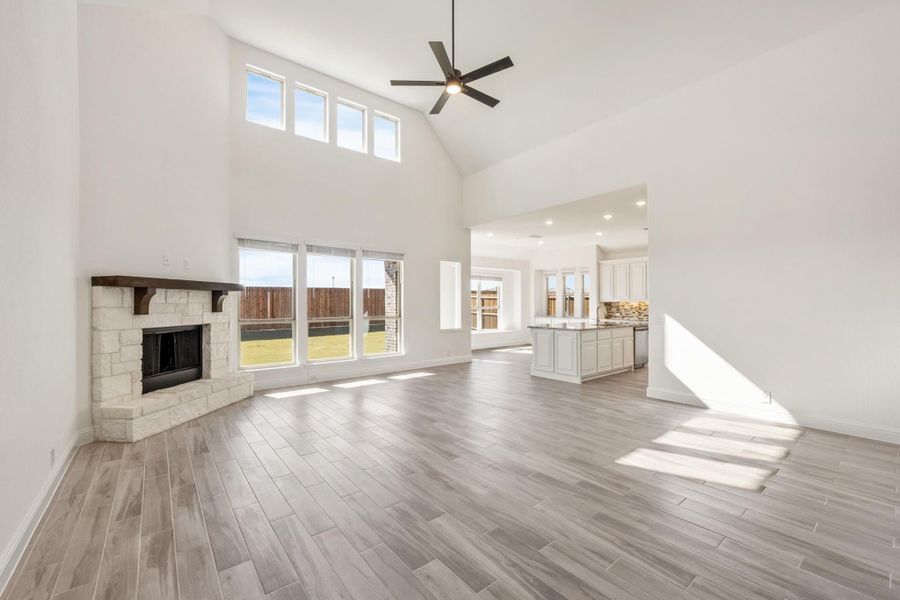 Open living room with vaulted ceiling, stone fireplace, ceiling fan, and wood-look floors open to kitchen Open living room with vaulted ceiling, stone fireplace, ceiling fan, and wood-look floors open to kitchen