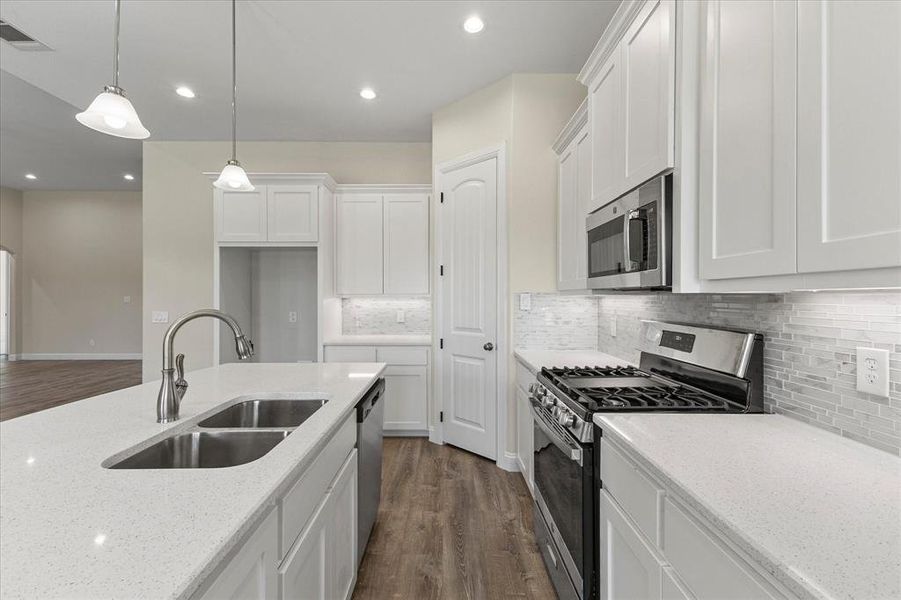 Kitchen with stainless steel appliances, dark wood-type flooring, white cabinets, light stone countertops, and backsplash