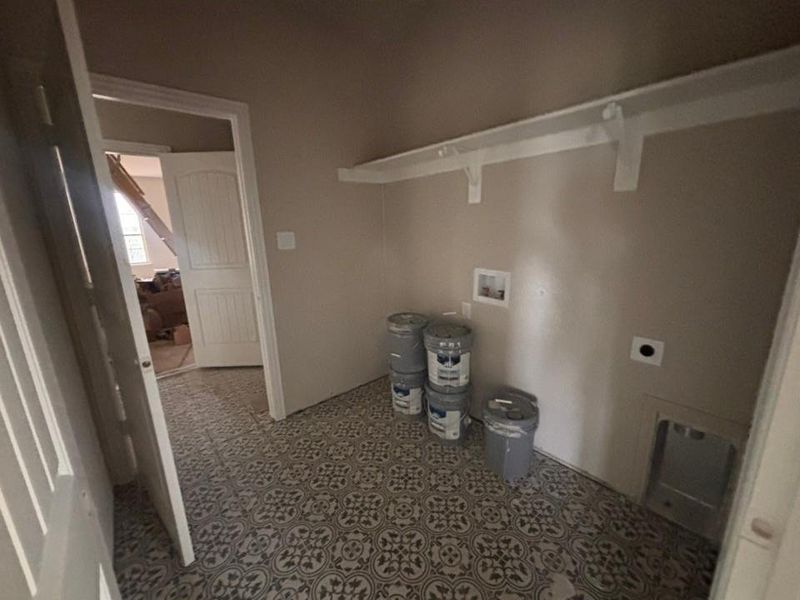 Laundry area featuring patterned floor tile, overhead shelving, and utility hookups for appliances