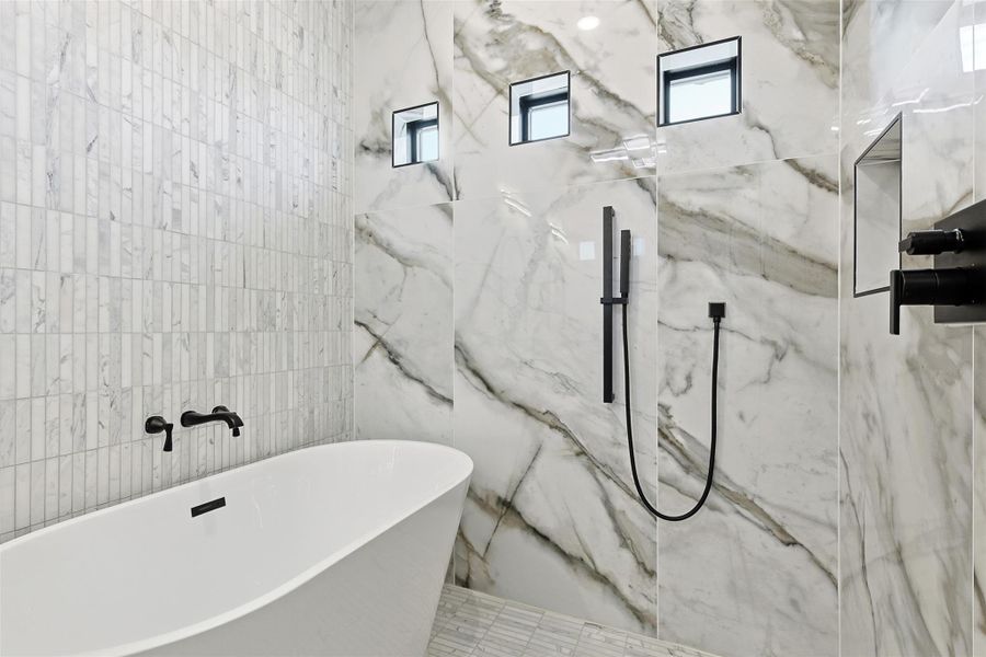 A standalone soaking tub is paired with matte black wall-mounted fixtures and marble-look tile walls.