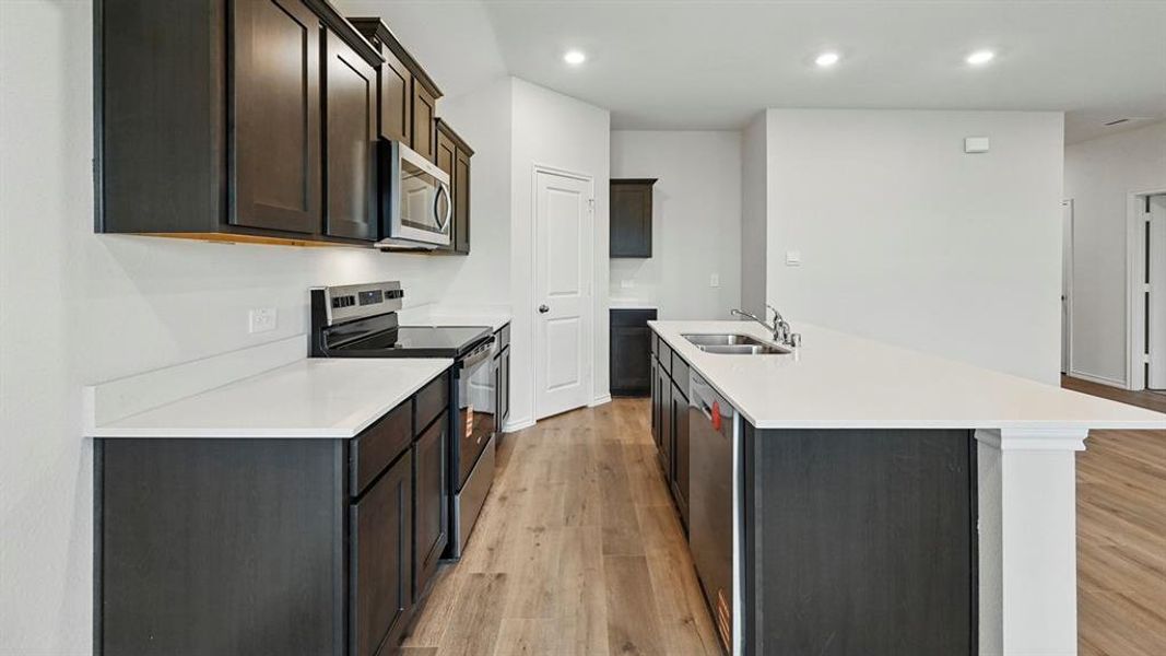 Kitchen featuring stainless steel appliances, light wood-type flooring, recessed lighting, an island with sink, and light stone counters