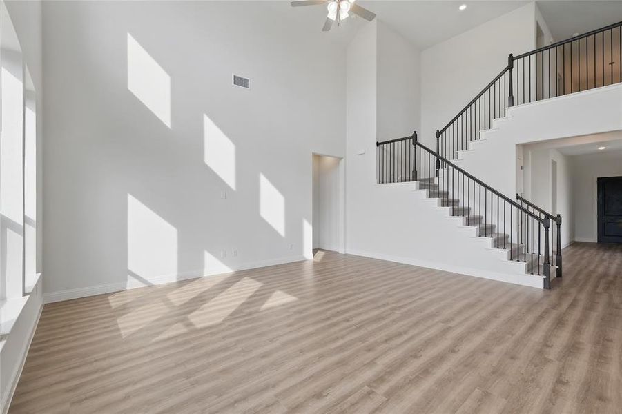 Unfurnished living room with stairs, a high ceiling, visible vents, and light wood finished floors Unfurnished living room with stairs, a high ceiling, visible vents, and light wood finished floors