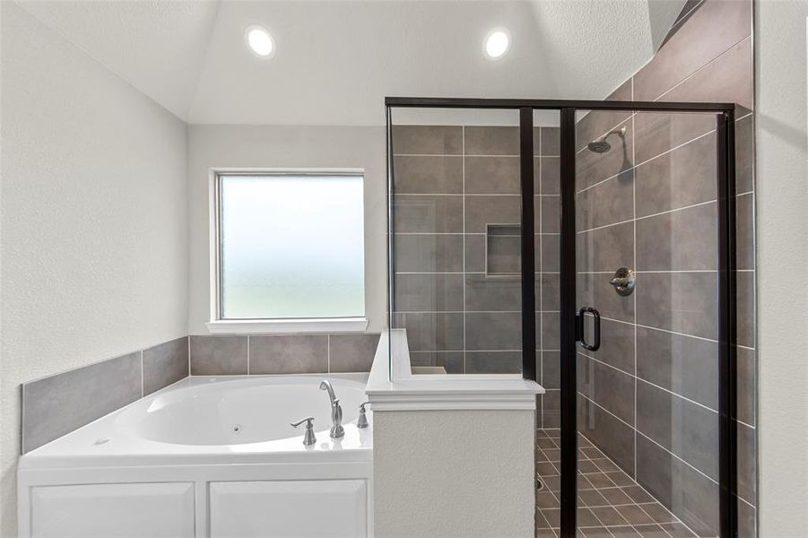 Soaking tub with chrome fixtures, enclosed shower with dark-framed glass, recessed shower niche, and tiled walls
