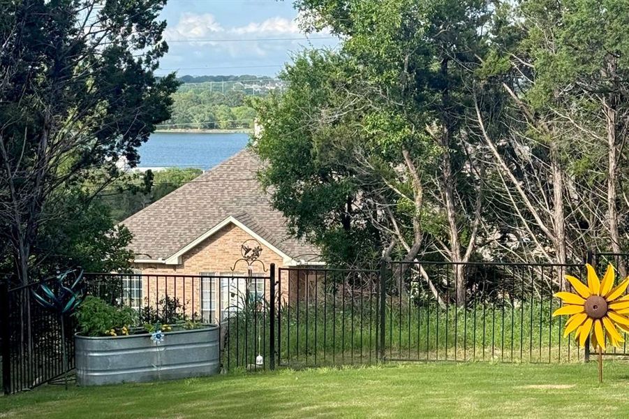 Expansive green lawn with a black metal fence, mature perimeter trees, and a distant body of water
