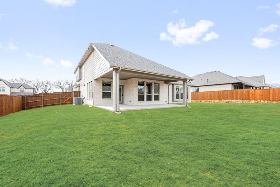 Backyard of two-story brick home with covered patio, large green lawn, and wood privacy fence