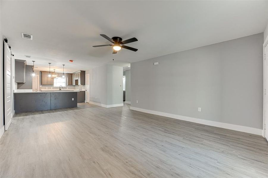 Unfurnished living room with a barn door, sink, ceiling fan with notable chandelier, and light wood-type flooring