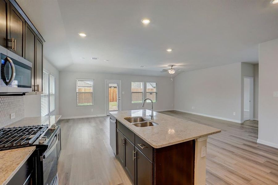 Kitchen featuring stainless steel appliances, a center island with sink, sink, decorative backsplash, and light wood-type flooring