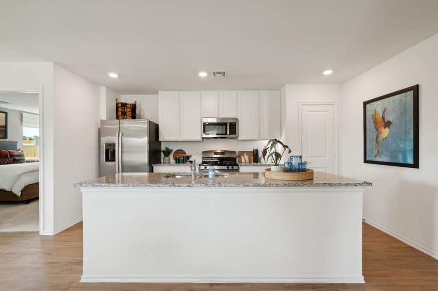 Kitchen featuring white cabinets, appliances with stainless steel finishes, light hardwood / wood-style flooring, and an island with sink