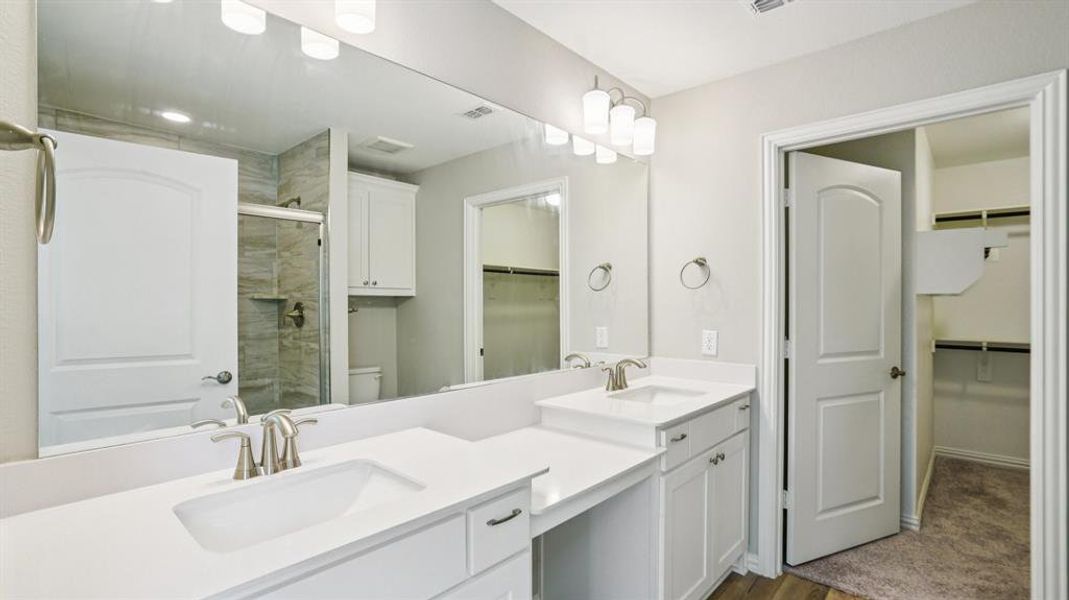 Full bath with a walk in closet, double vanity, a shower stall, and dark wood-style floors Full bath with a walk in closet, double vanity, a shower stall, and dark wood-style floors