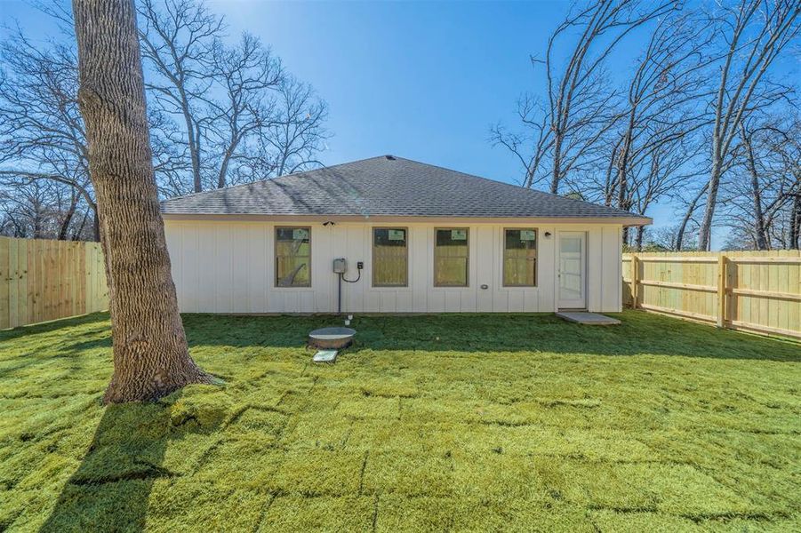 Back of property with a fenced backyard, a shingled roof, and a lawn