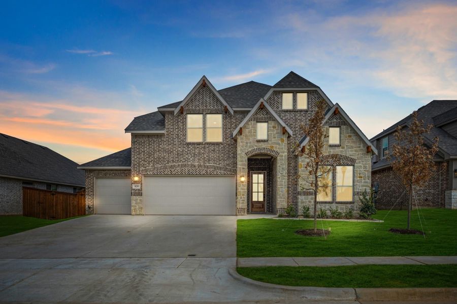 Two-story brick and stone home with two-car garage, arched entry, and green front lawn at dusk