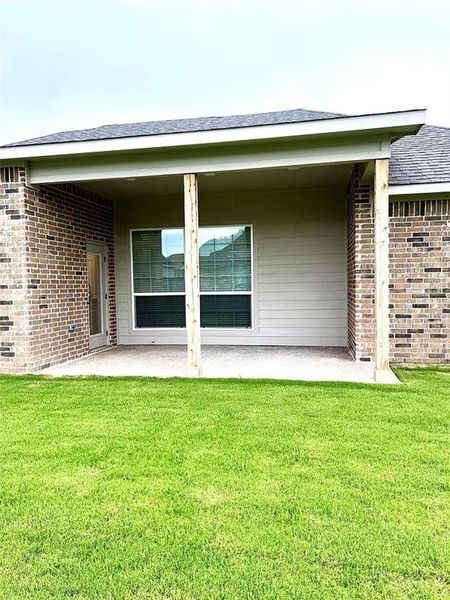 Covered patio with a concrete slab, supported by two wooden posts, extending from the rear of the brick exterior Covered patio with a concrete slab, supported by two wooden posts, extending from the rear of the brick exterior