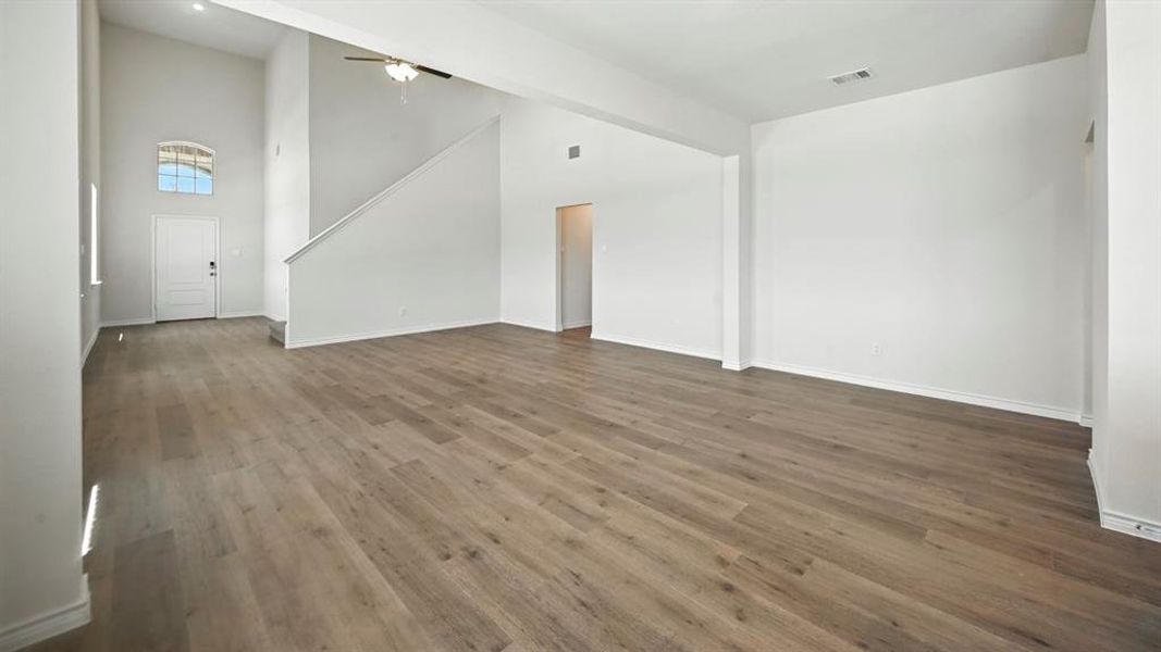 Unfurnished living room with a towering ceiling, wood finished floors, and a ceiling fan