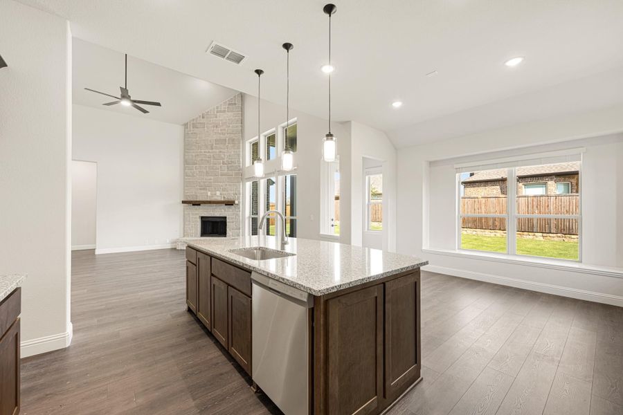 Open-concept kitchen with dark wood island, granite countertop, and pendant lights, overlooking living area with stone fireplace. Open-concept kitchen with dark wood island, granite countertop, and pendant lights, overlooking living area with stone fireplace.