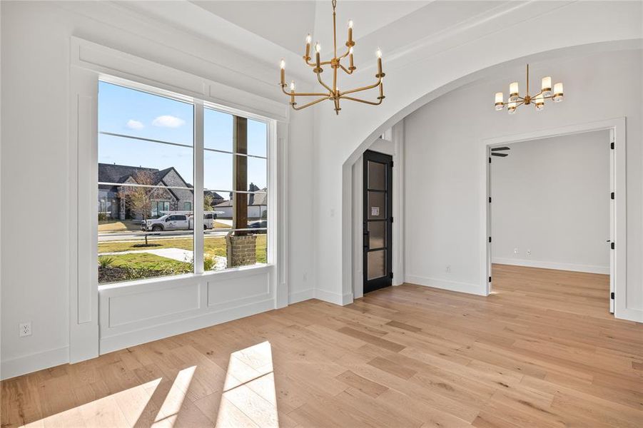 Unfurnished dining area with a chandelier, light wood-style flooring, and arched walkways Unfurnished dining area with a chandelier, light wood-style flooring, and arched walkways