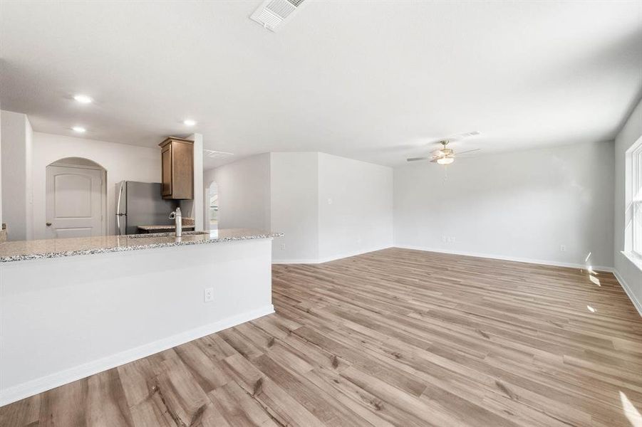 Kitchen featuring light wood-type flooring, light stone counters, ceiling fan, stainless steel fridge, and sink