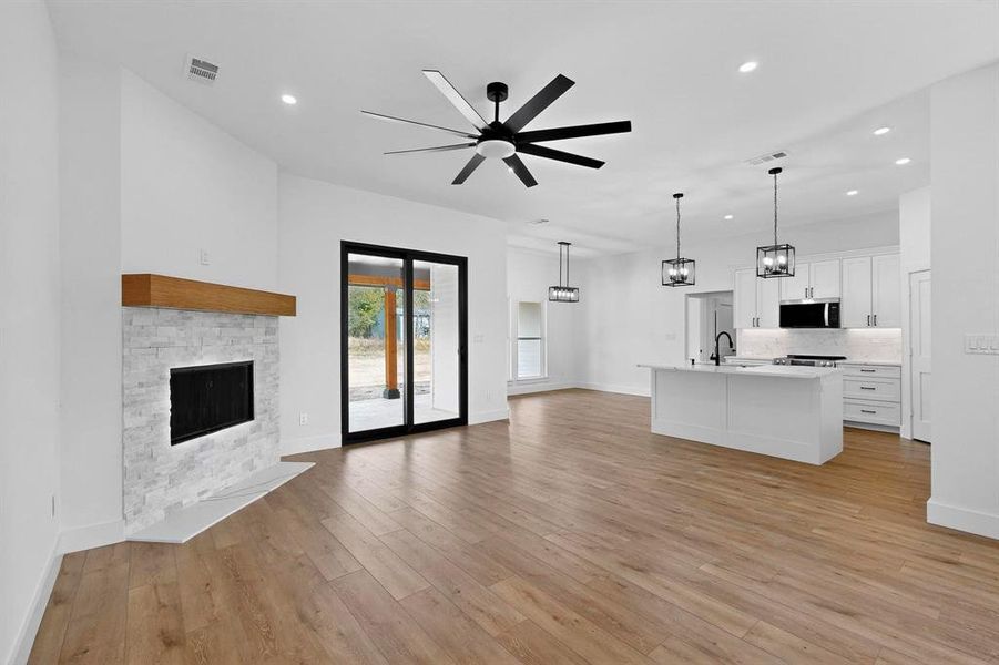 Unfurnished living room with recessed lighting, light wood-style flooring, a stone fireplace, a chandelier, and a ceiling fan