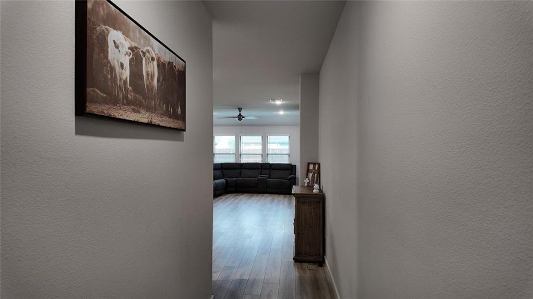 Hallway featuring light-colored walls and wood-style flooring, leading to a living area with large windows