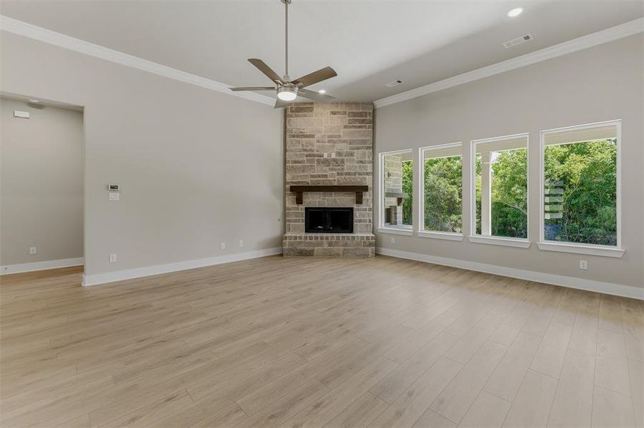 Spacious living area featuring wood-finish flooring, a stone-clad corner fireplace with a wooden mantel, and multiple large windows