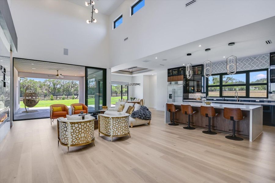 Living room with light wood floors and a towering ceiling, fireplace and doors that open up along the back of the house/patio Living room with light wood floors and a towering ceiling, fireplace and doors that open up along the back of the house/patio