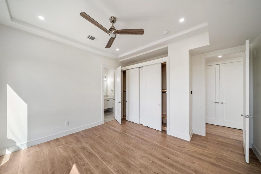 Secondary bedroom features wood floors, a ceiling fan, recessed lighting, and ample closet space with sliding doors. Natural light enhances the neutral color scheme, creating a bright and airy atmosphere.